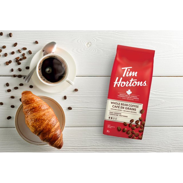 Tim Hortons Original Blend whole bean coffee bag beside a cup of black coffee and croissant on a white table