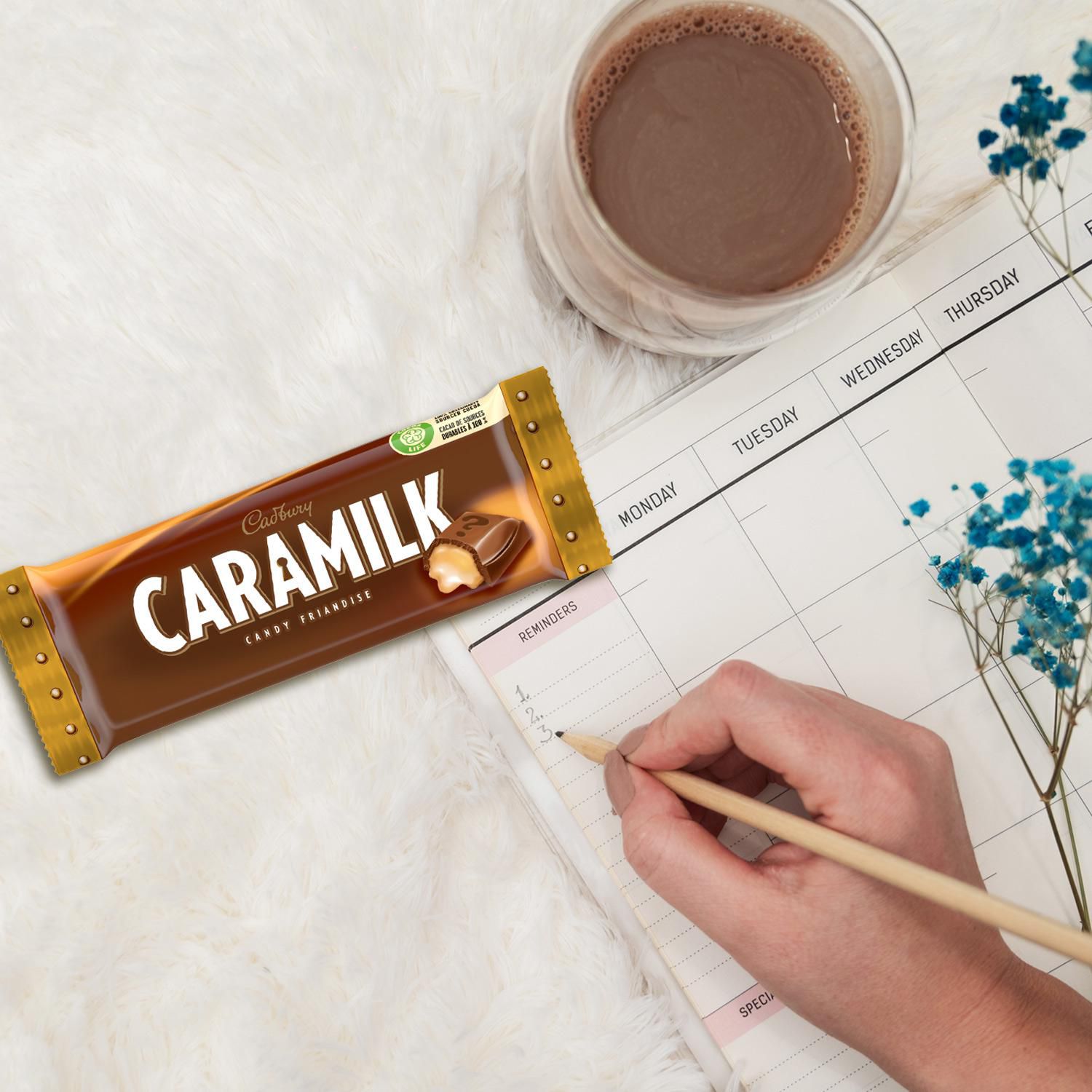 Cadbury Caramilk 50g bar placed beside a weekly planner and cup of chocolate drink