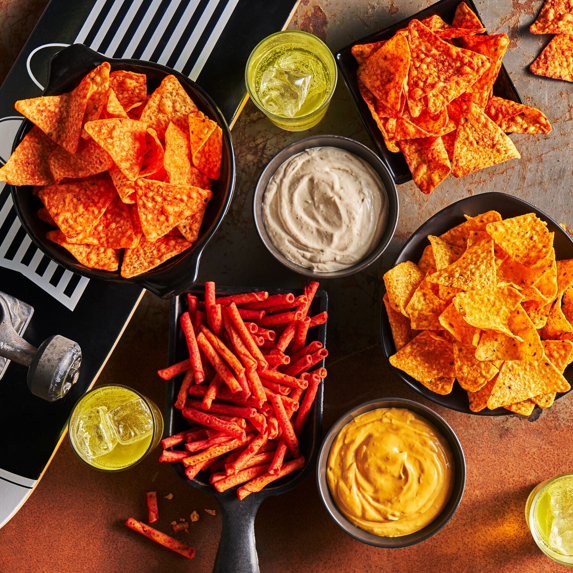 Assorted seasoned tortilla chips and crunchy snacks served in bowls with dips and drinks