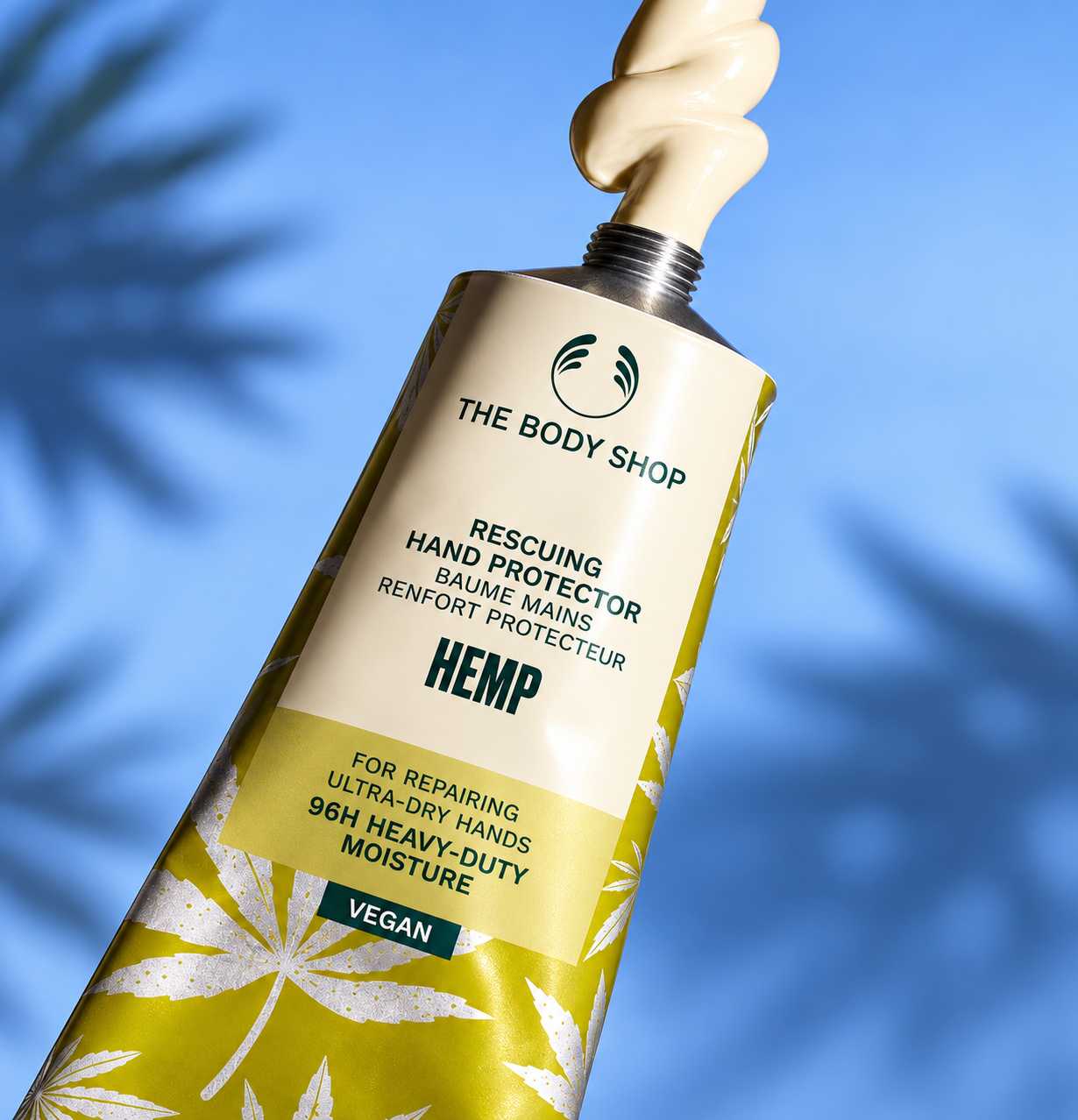 The Body Shop Hemp Hand Protector tube dispensing rich hand cream against a blue background